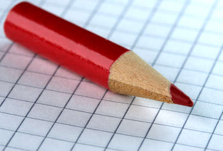 An old small used sharpened red wooden slate pencil lies on a checkered paper sheet, close-upの写真素材
