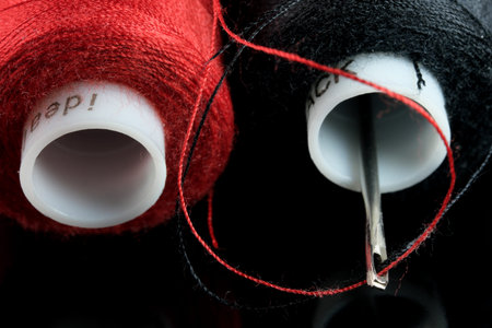 Spools of red and black thread and an inserted needle with thread on a black background close-up...