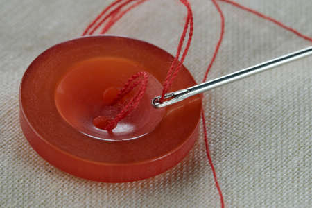 Red button with a needle with inserted thread on a white linen cloth close-up macro photographyの写真素材