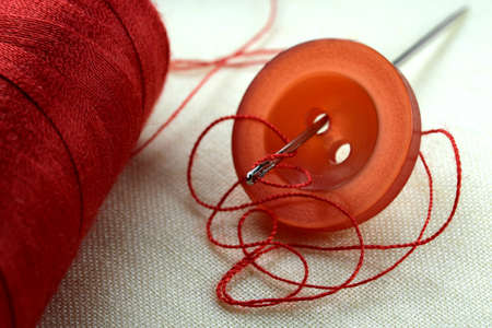 Red button with a needle with inserted thread on a white linen cloth close-up macro photographyの写真素材