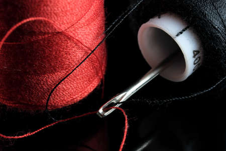 Spools of red and black thread and an inserted needle with thread on a black background close-up macro photographyの写真素材