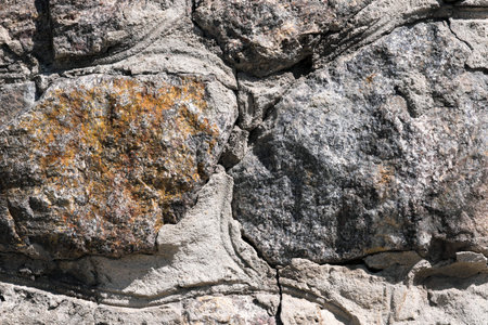 Background of stone granite masonry with natural stones close-up brightly lit by the sun