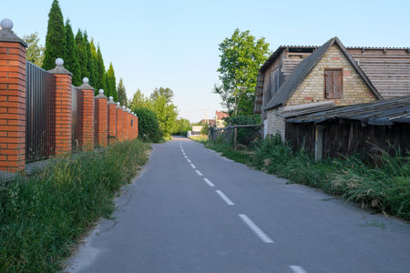 Summer rural landscape with modern cottage buildings and fences along an asphalt road