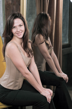 Portrait of a young attractive brunette girl in a leather light top next to a mirror close-upの写真素材