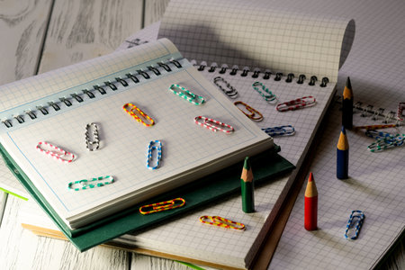 Opened blank notepads with checkered loose-leaf papers with pencils and paper clips in twilight light stationery educational backgroundの写真素材