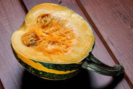A small sweet ripe cut pumpkin lies on a brown wooden table close-upの写真素材