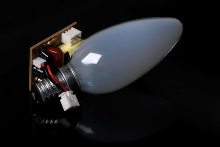 Base light incandescent lamp next to electronic circuit boards on a black mirror background