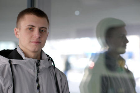 Portrait of a young handsome guy with a short haircut on the street of the spring city close-up next to the glass showcase of the storeの写真素材