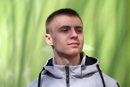 Portrait of a young handsome guy on a green background, in the bright spring sun, close-up