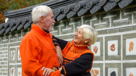 Elderly gray-haired optimistic couple man and woman against the backdrop of a Japanese garden wall...