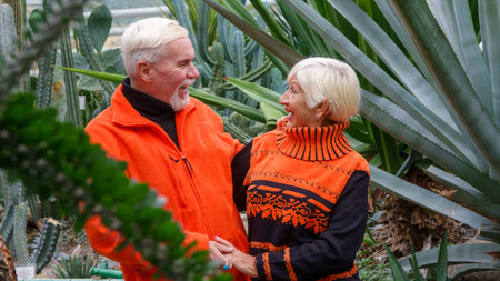 Elderly gray-haired optimistic couple in love man and woman against the background of green plants...