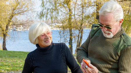 Portrait of an elderly gray-haired couple, a man in military khaki clothes, a woman in a black sweater, with an orange smartphoneの写真素材