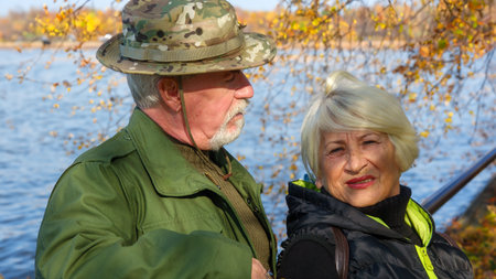 Portrait of an elderly gray-haired couple, a man in militarized khaki clothes, a woman in a black windbreaker, in autumn in the city on the embankment of the riverの写真素材