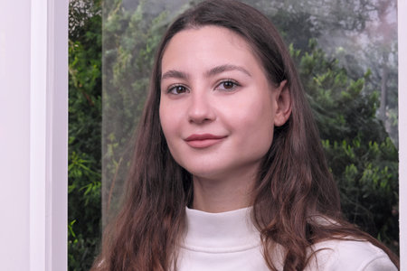 Portrait of a beautiful cute young woman in a white sweater against the background of a window