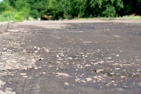 Damaged road pavement, potholes and pits in the city after rain on a summer dayの写真素材