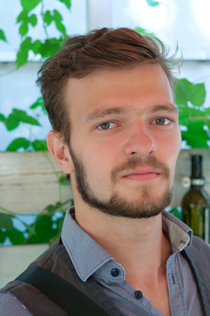Street portrait of a young handsome man with a small beard and mustache sits at a table in a summer...
