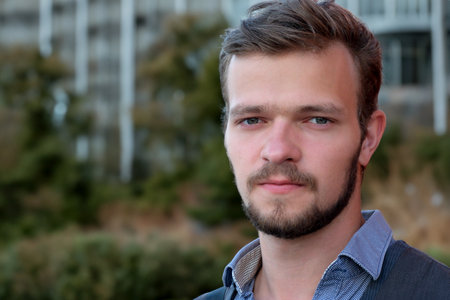 Street portrait of a young handsome man with a small beard and mustache in a vest on a warm summer dayの写真素材