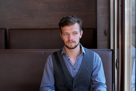 Street portrait of a young handsome man with a small beard and mustache sits at a table in a summer cafeの写真素材