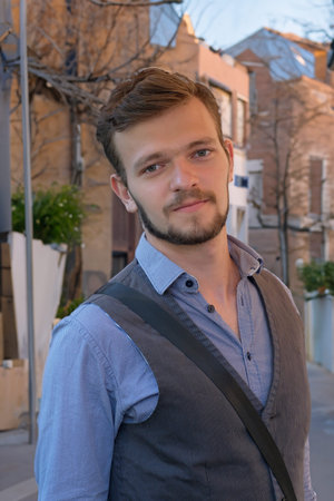 Street portrait of a young handsome man with a small beard and mustache in a vest on a warm summer...