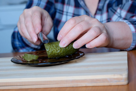 The hands of an elderly woman take out delicious home-made pickled cucumbers from a jar for cutting...