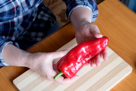 Hands of an elderly woman showing red bell peppers in the kitchen at a brown table, no face, close-upの写真素材