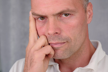 Portrait of a young man with a short haircut in a white raglan on a gray background, close-up.