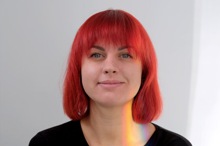 A young attractive woman with a short orange hairstyle in a black T-shirt and jeans posing in the studio on a white background.の写真素材