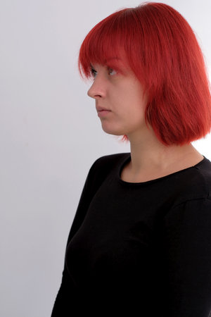 A young attractive woman with a short orange hairstyle in a black T-shirt and jeans posing in the studio on a white background.の写真素材