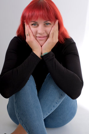 A young attractive woman with a short orange hairstyle in a black T-shirt and jeans posing in the studio on a white background.の写真素材