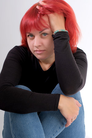 A young attractive woman with a short orange hairstyle in a black T-shirt and jeans posing in the studio on a white background.の写真素材
