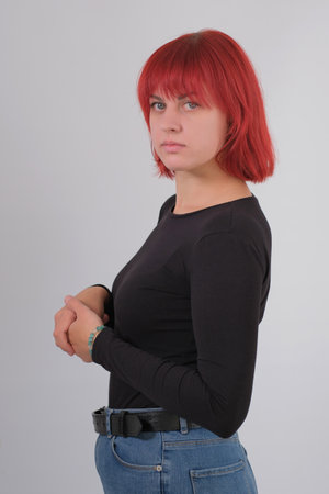 A young attractive woman with a short orange hairstyle in a black T-shirt and jeans posing in the studio on a white background.の写真素材