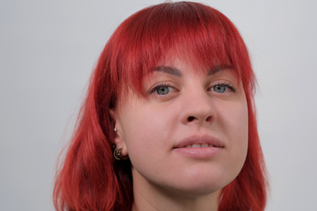 A young attractive woman with a short orange hairstyle in a black T-shirt and jeans posing in the studio on a white background.の写真素材