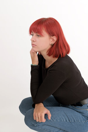 A young attractive woman with a short orange hairstyle in a black T-shirt and jeans posing in the studio on a white background.の写真素材
