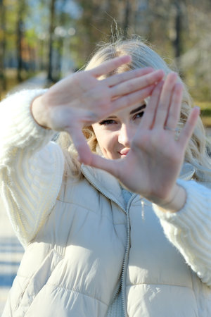 Portrait of a young beautiful blonde with long hair in a white sweater and jacket in sunny autumn in a city parkの写真素材