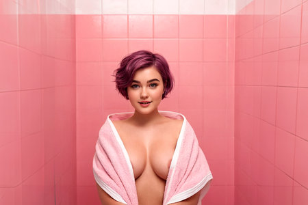 Young pretty attractive woman posing with a towel in a stylish pink bathroom. AI generated.の素材