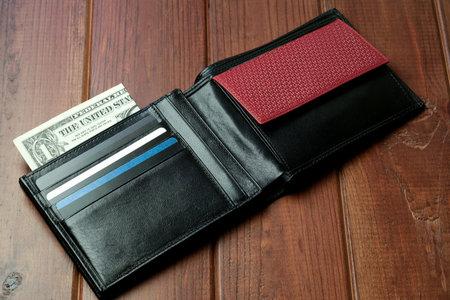 An elegant black wallet reveals a single dollar bill and several cards nestled within it.