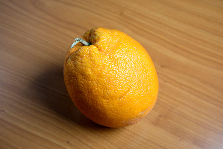 A plump orange lies on a smooth wooden surface, perfect for snacking.