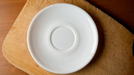 A simple white plate rests on a textured wooden surface, creating calmness.の写真素材