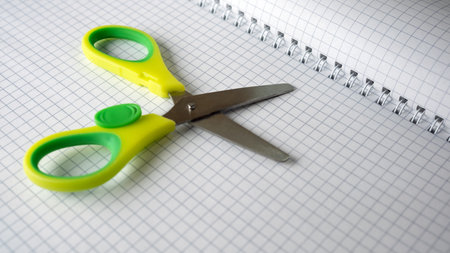Bright green scissors lie next to a grid patterned notebook, ready for use.