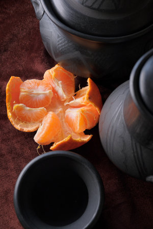 Vibrant orange slice rests near unique clay pottery on textured fabric.の写真素材