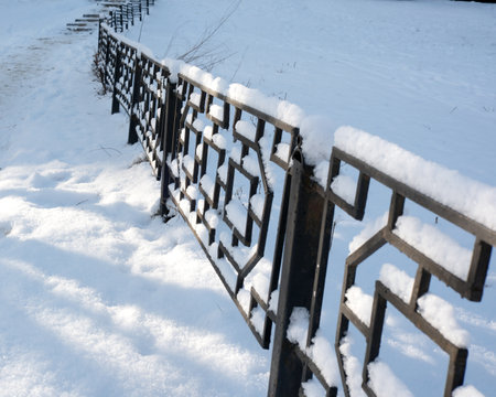 A quiet winter day features a snow-laden fence and soft sunlight.の写真素材