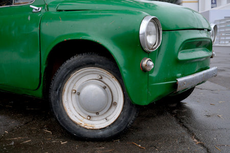 A classic green car sits quietly on a wet city street during rain.の写真素材