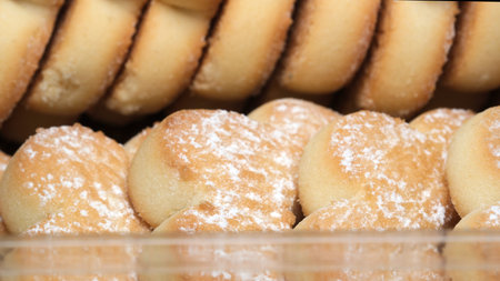 Warm, golden cookies dusted with powdered sugar are neatly stacked in a clear container. The...