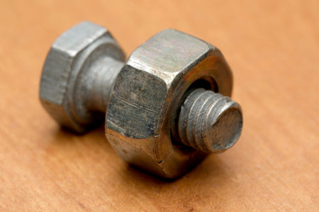 Close-up of a shiny metal bolt intertwined with a nut on wood.