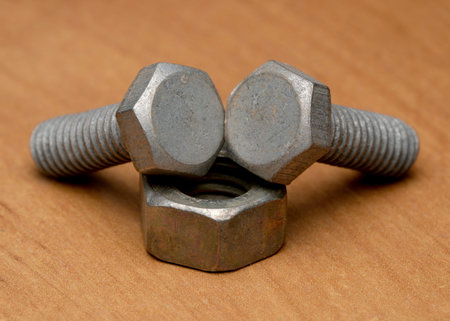 Three metallic bolts and a nut are creatively displayed on a wooden background.