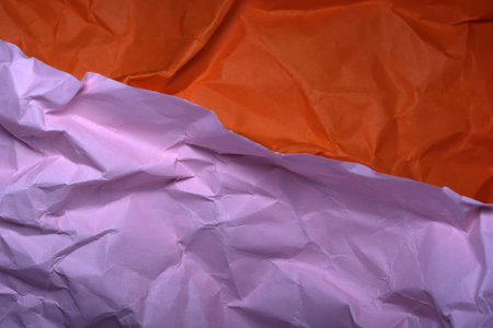 The bright orange and soft pink paper lie crumpled together, showing depth.