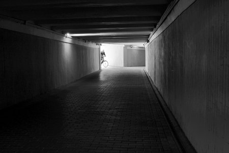 A solitary cyclist rides through a dim tunnel as evening light beckons from the end.の写真素材