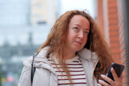 A woman strolls through an urban area, absorbed in her mobile device.