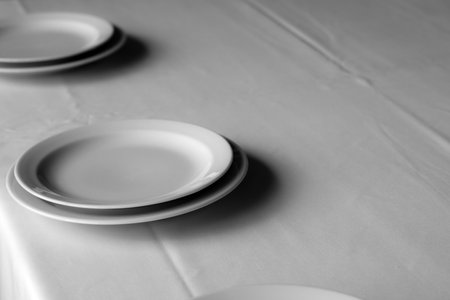 Neatly arranged white plates rest on a crisp tablecloth, ready for dinner guests.の写真素材