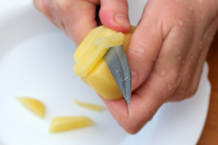 Hands skillfully peel fresh potatoes in a sunlit kitchen filled with warmth.の写真素材